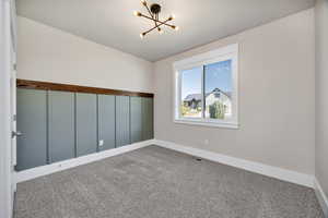 Carpeted spare room with a chandelier and baseboards