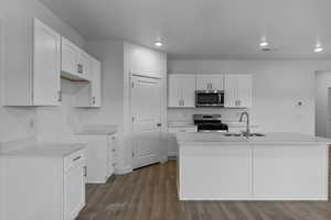 Kitchen featuring white cabinets, dark wood-type flooring, stainless steel appliances, a center island with sink, and recessed lighting