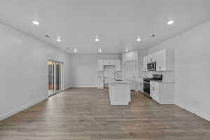 Kitchen with white cabinetry, stainless steel appliances, a kitchen island with sink, recessed lighting, and light wood-type flooring