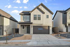View of front of home featuring stone siding, an attached garage, concrete driveway, and board and batten siding