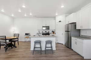 Kitchen featuring white cabinetry, light wood-style floors, stainless steel appliances, a center island with sink, and recessed lighting