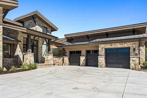 View of front of home with a standing seam roof, stone siding, a metal roof, driveway, and a garage