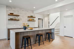 Kitchen featuring open shelves, a kitchen breakfast bar, tasteful backsplash, recessed lighting, and light stone counters