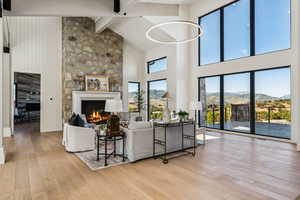 Living area featuring a mountain view, high vaulted ceiling, light wood-type flooring, beam ceiling, and a warm lit fireplace