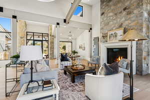 Living area with high vaulted ceiling, light wood-style floors, a warm lit fireplace, a chandelier, and beam ceiling