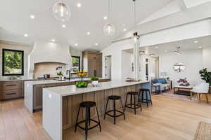 Kitchen featuring recessed lighting, a kitchen breakfast bar, light stone countertops, pendant lighting, and vaulted ceiling