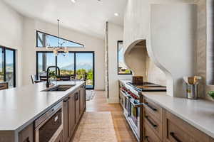 Kitchen featuring appliances with stainless steel finishes, decorative light fixtures, light wood-style flooring, a mountain view, and a kitchen island with sink