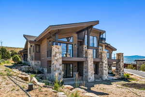 Rear view of property featuring stone siding, a mountain view, and a balcony