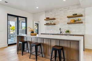 Bar area with open shelves, decorative backsplash, recessed lighting, light stone countertops, and light wood-style flooring