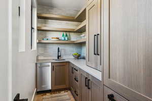 Bar area with open shelves, tasteful backsplash, brown cabinetry, light wood-style flooring, and light stone counters