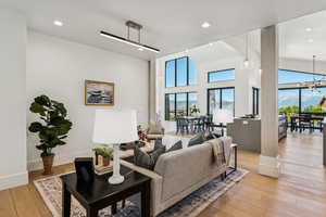 Living area featuring light wood finished floors, healthy amount of natural light, recessed lighting, a high ceiling, and a chandelier
