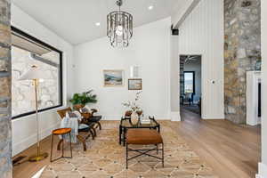 Sitting room with light wood-type flooring, healthy amount of natural light, high vaulted ceiling, and a chandelier