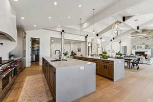 Kitchen with open floor plan, light stone countertops, hanging light fixtures, double oven range, and light wood-style flooring