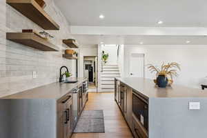 Kitchen with light stone countertops, light wood-style flooring, open shelves, appliances with stainless steel finishes, and recessed lighting