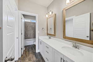Bathroom with double vanity, dark wood-style floors, and shower / bathtub combination