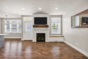 Unfurnished living room with dark wood-type flooring, a fireplace, a textured ceiling, and hanging lights