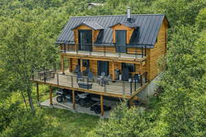 Back of house with a standing seam roof, a wooden deck, log exterior, and a forest view