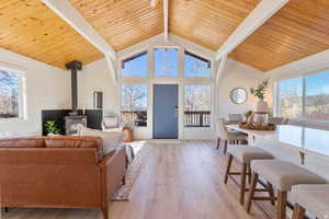 Living room featuring a wood stove, wooden walls, a high wooden beamed ceiling, light wood-type flooring, and plenty of natural light