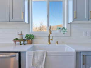 Kitchen view of stainless steel dishwasher, light stone counters, and white cabinetry