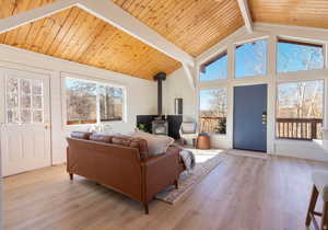 Living area with a wood stove, a high wooden beamed ceiling, light wood-type flooring, and wooden walls
