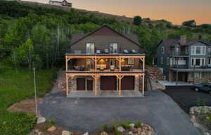 Back of property at dusk with stone siding, a garage, asphalt driveway, and a balcony