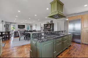 Kitchen with green cabinetry, stainless steel appliances, a kitchen island, recessed lighting, and open floor plan