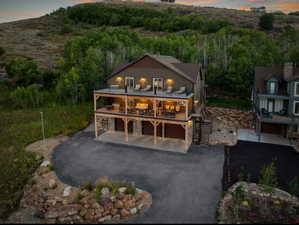 Back of house at dusk with stone siding, driveway, a patio area, a garage, and a balcony