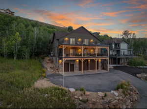 Back of property at dusk with stone siding, asphalt driveway, an attached garage, and a patio area