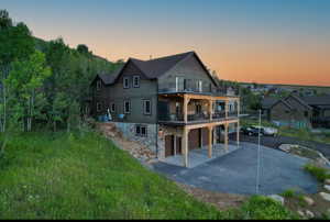 Back of property with stone siding, a patio area, an attached garage, driveway, and a balcony