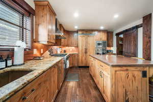 Kitchen with a barn door, built in appliances, dark wood-style flooring, recessed lighting, and a center island