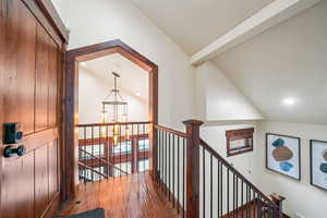 Hallway featuring lofted ceiling with beams, hardwood / wood-style floors, an upstairs landing, and suspended lighting