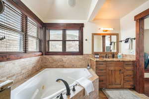 Bathroom featuring vanity, a tub with jets, and lofted ceiling