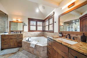 Full bathroom featuring vaulted ceiling, two vanities, a jetted tub, a stall shower, and tile walls