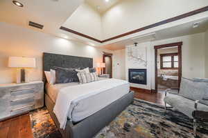 Bedroom with dark wood-type flooring, a glass covered fireplace, and a raised ceiling