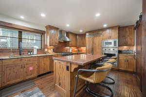 Kitchen featuring stainless steel appliances, a breakfast bar area, dark wood-style flooring, a kitchen island with sink, and wood finish cabinetry