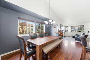 Dining room with dark wood-type flooring, vaulted ceiling, and a chandelier