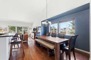 Dining room featuring lofted ceiling, dark wood-style floors, a chandelier, and healthy amount of natural light