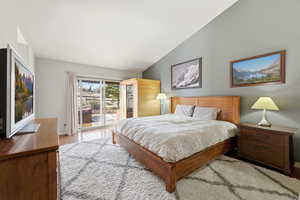 Bedroom with access to exterior, light wood-style floors, and vaulted ceiling