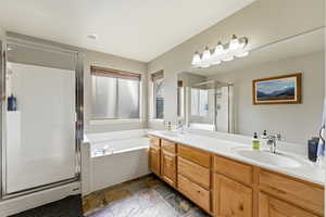Full bathroom featuring a stall shower, stone tile floors, double vanity, and a garden tub