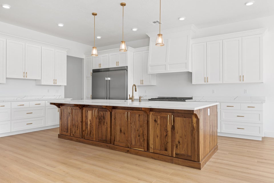 Dual tone kitchen featuring a center island with sink, two tone cabinets, light wood finished floors, built in refrigerator, and hanging light fixtures
