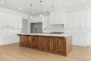 Dual tone kitchen featuring a center island with sink, two tone cabinets, light wood finished floors, built in refrigerator, and hanging light fixtures