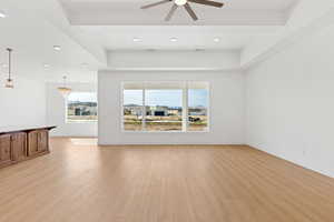 Unfurnished room featuring plenty of natural light, ceiling fan, light wood-style floors, a raised ceiling, and recessed lighting