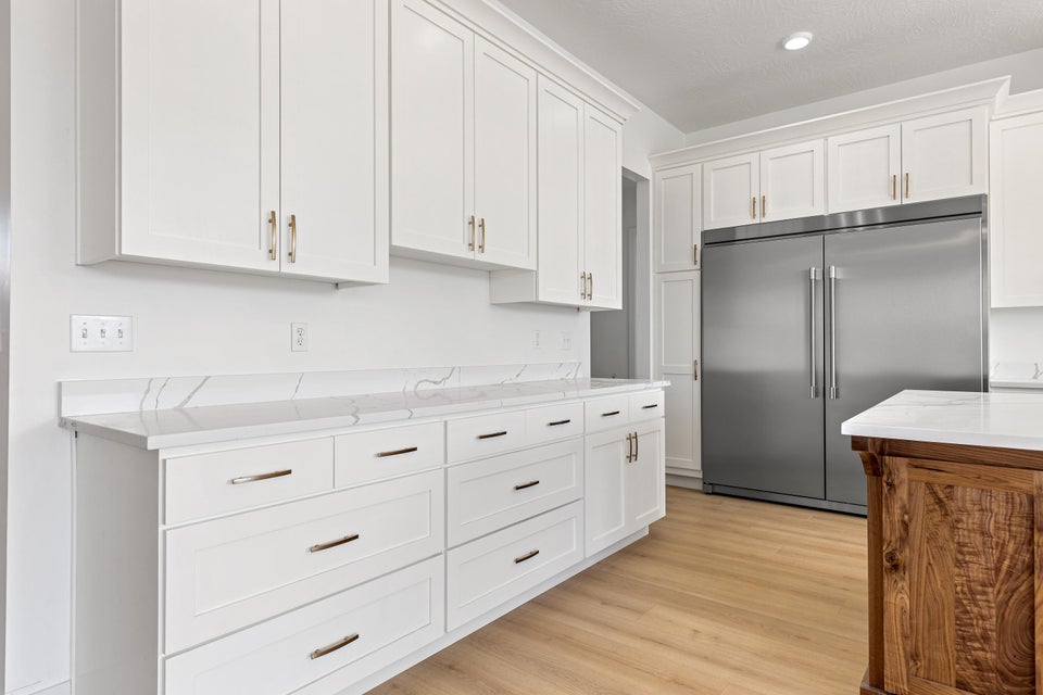 Kitchen with built in fridge, white cabinets, light wood-style flooring, and light stone countertops
