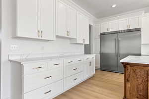 Kitchen with built in fridge, white cabinets, light wood-style flooring, and light stone countertops