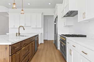 Two tone kitchen with high end appliances, light stone countertops, a kitchen island with sink, two tone color scheme, and decorative light fixtures