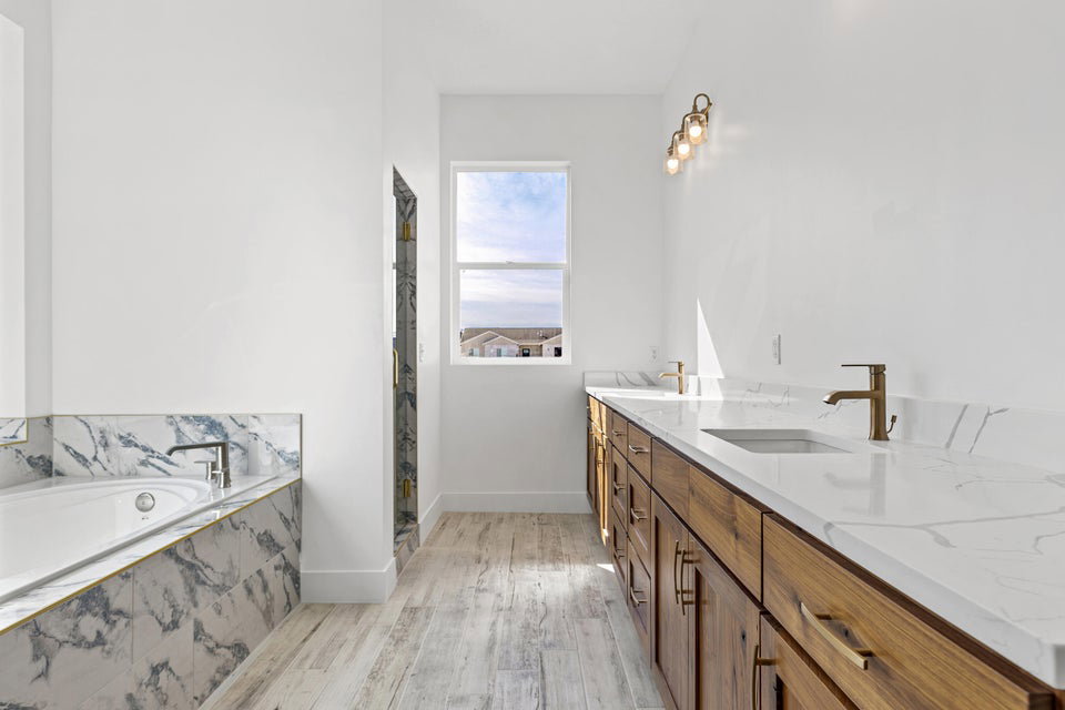Bathroom featuring double vanity, light wood-type flooring, a garden tub, and a marble finish shower