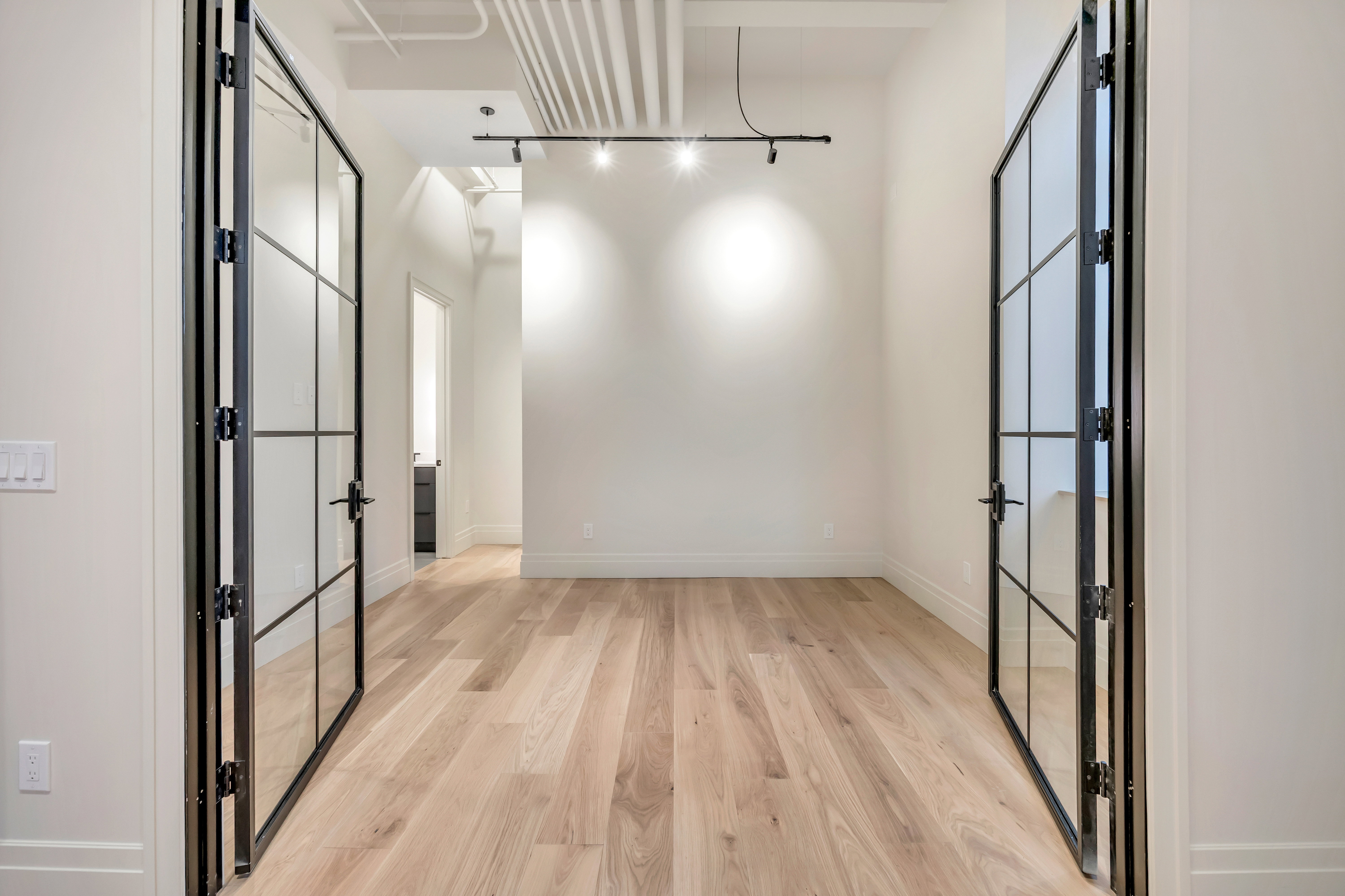 Empty room featuring light wood-style flooring, rail lighting, and french doors
