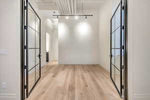 Empty room featuring light wood-style flooring, rail lighting, and french doors