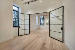 Empty room featuring light wood finished floors, rail lighting, and a high ceiling