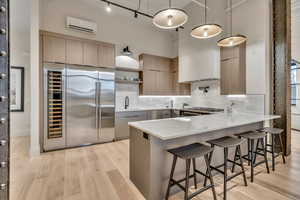 Kitchen featuring a peninsula, stainless steel appliances, a breakfast bar, light stone countertops, and light wood-style floors